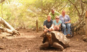 3 personas, una de ellas usuaria de silla de ruedas, junto a una tortuga gigante en Galápagos