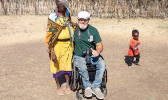 Usuario de silla de ruedas posando en un poblado Masai con una mujer y un niño jugando