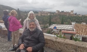 Un usuario de silla de ruedas con su esposa y al fondo la Alhambra