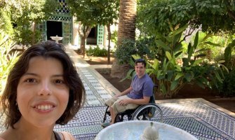 Una selfie con una chica en primer plano y un usuario en silla de ruedas al fondo en un patio de un alojamiento en Marrakech 