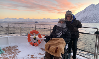 Dos viajeros, uno usuario de silla de ruedas, desde la proa de un barco con nieve durante una navegación en el fiordo de Tromso