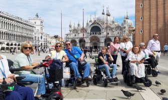 Grupo de viajeros usuarios de silla de ruedas disfrutando de un viaje adaptado en la plaza de San Marcos en Venecia