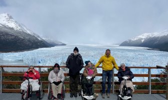Un grupo de usuarios de silla de ruedas y al fondo se ve el glaciar perito moreno