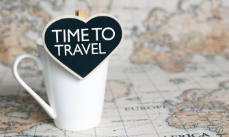 Imagen de un mapa del mundo con una taza y un cartel que dice en ingles: tiempo de viajar