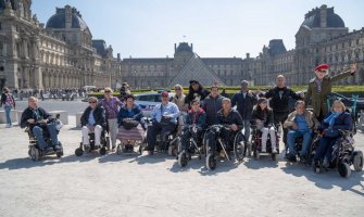 Grupo de viajeros usuarios de silla de ruedas en París con la pirámide del museo del Louvre al fondo