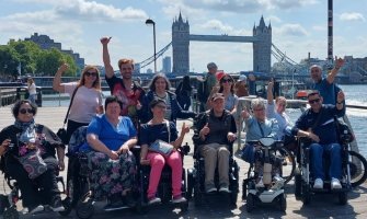 Un grupo de usuarios de silla de ruedas en un viaje a Londres, al fondo se puede ver el Tower Bridge